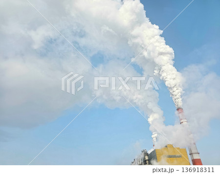 Thick white smoke plumes rise from industrial chimneys against a clear blue sky. Environmental pollution and global warming concept. Thick white smoke plumes rise from industrial chimneys against a clear blue sky. Environmental pollution and global warming concept. 136918311