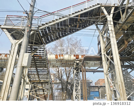 Industrial scene with an old, weathered pedestrian bridge and utility pole showing exposed wires and pipes covered with snow in winter. Industrial scene with an old, weathered pedestrian bridge and utility pole showing exposed wires and pipes covered with snow in winter. 136918312