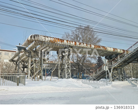 Elevated pipes with insulation damage and power lines above a snowy urban landscape, showcasing industrial infrastructure in winter. 136918313