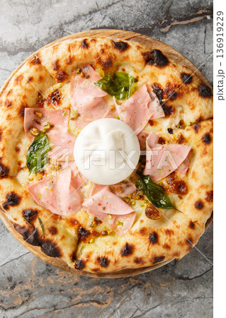 Charred pizza with mortadella sausage and burrata cheese close-up on a wooden board. Vertical top view 136919229