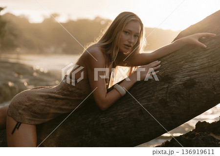 Portrait of blonde woman posing on wooden log at beach Portrait of blonde woman posing on wooden log at beach 136919611