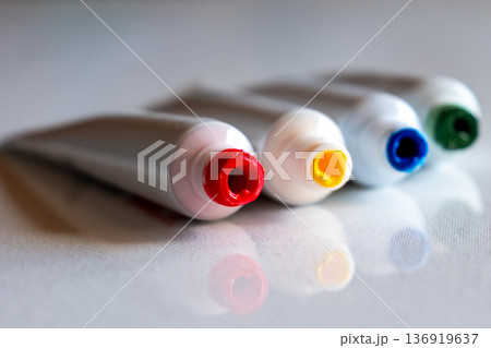 A row of paint tubes in various colors including red, yellow, green, and blue. The tubes are arranged neatly on a white surface, showcasing their vibrant caps. 136919637