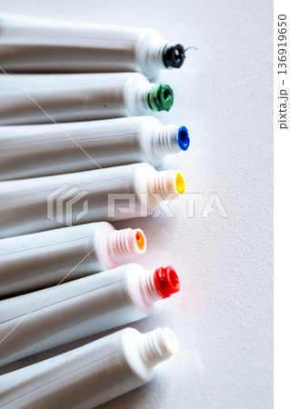 A row of paint tubes in various colors including red, yellow, green, and blue. The tubes are arranged neatly on a white surface, showcasing their vibrant caps. A row of paint tubes in various colors including red, yellow, green, and blue. The tubes are arranged neatly on a white surface, showcasing their vibrant caps. 136919650