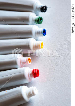A row of paint tubes in various colors including red, yellow, green, and blue. The tubes are arranged neatly on a white surface, showcasing their vibrant caps. A row of paint tubes in various colors including red, yellow, green, and blue. The tubes are arranged neatly on a white surface, showcasing their vibrant caps. 136919651