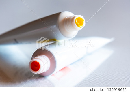 Two tubes of paint, one yellow and one red, are placed on a reflective surface. The caps are visible, showcasing the vibrant colors. 136919652