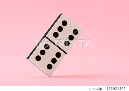 Domino tile stands on its edge against a pink background in a simple display of balance 136921565