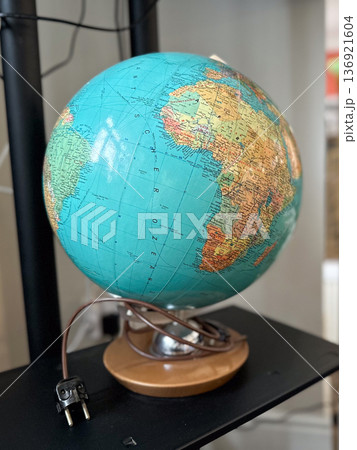 Rotating world globe with electric cord placed on dark shelf in retro interior. Travel, geography, exploration, and global education 136921604