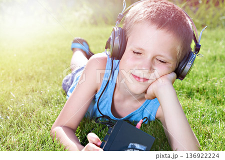Little boy lying on grass with old audio cassette player Little boy lying on grass with old audio cassette player 136922224