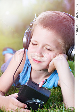 Little boy lying on grass with old audio cassette player 136922225