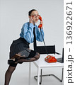 Young calm white woman in office attire working talking on vintage red phone, isolated on white background. In a blue shirt with a tie. Business occupation. 136922671