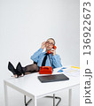 Young calm white woman in office attire working on laptop while talking on vintage red phone, isolated. Business occupation. In a blue shirt with a tie. Freelance . relaxation 136922673