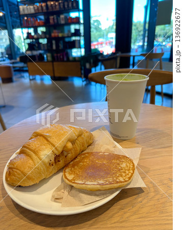 Cozy breakfast scene with a croissant, pancake and matcha latte served on a wooden table. Blurred background of a cafe adds depth and evokes a sense of warmth and relaxation in a casual dining setting Cozy breakfast scene with a croissant, pancake and matcha latte served on a wooden table. Blurred background of a cafe adds depth and evokes a sense of warmth and relaxation in a casual dining setting 136922677