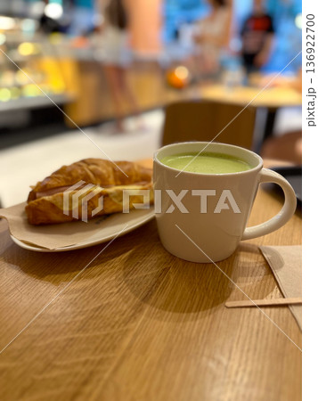 Cup of matcha latte and a croissant on a wooden table in a cozy cafe or coffee shop. Warmth and comfort of a morning or afternoon break. Cup of matcha latte and a croissant on a wooden table in a cozy cafe or coffee shop. Warmth and comfort of a morning or afternoon break. 136922700