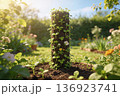 Sunlit garden features a cylindrical soil tower covered with seedlings and tiny blossoms. 136923741