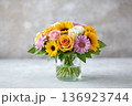 Cheerful mixed bouquet of sunflowers, roses and gerberas arranged in a clear glass jar with water 136923744