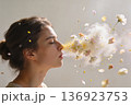 Side profile of a person exhaling a burst of petals, pollen, and soft smoke as daisies bloom in midair 136923753