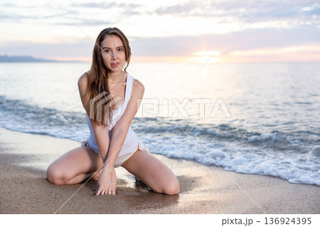 Girl sitting at sand at sea shore at sunset Girl sitting at sand at sea shore at sunset 136924395