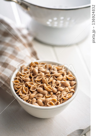 Wholegrain conchiglie pasta in bowl on white table. Wholegrain conchiglie pasta in bowl on white table. 136924832