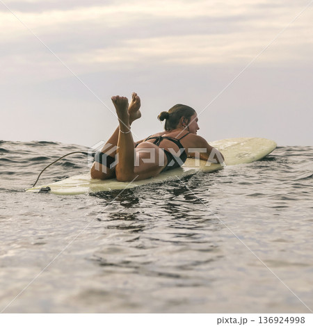 Female Comfortably Lying On Board Amidst Evening Waves And Sky 136924998