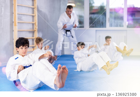 Teens in martial arts attire practicing abdominal crunches combined with hand strikes Teens in martial arts attire practicing abdominal crunches combined with hand strikes 136925380