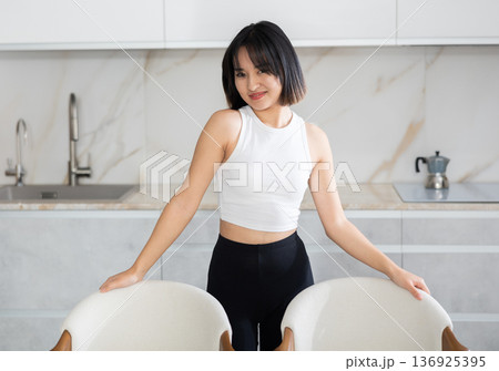 Smiling young Asian girl standing at table in the kitchen 136925395