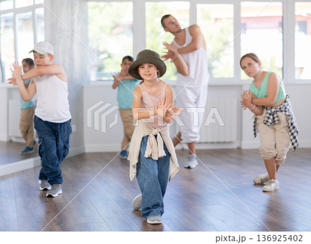In sports studio, childrens team learns hip-hop dance accompanied by experienced man teacher In sports studio, childrens team learns hip-hop dance accompanied by experienced man teacher 136925402