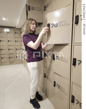 A woman uses a digital keypad to open a metal locker in a modern storage room, security facility, personal belongings, public space. A woman uses a digital keypad to open a metal locker in a modern storage room, security facility, personal belongings, public space. 136925425