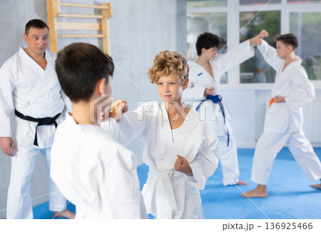 Diligent preteen attendee of karate classes fighting with his opponent in sports hall 136925466