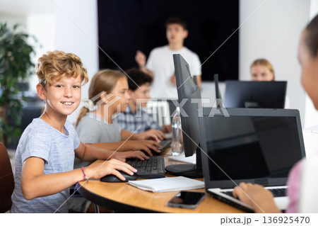 Smiling preteen boy sitting at computer table in training room Smiling preteen boy sitting at computer table in training room 136925470