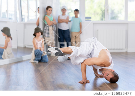 Experienced male trainer demonstrating to group of children dancers correct movements in hip-hop dance in choreography studio 136925477