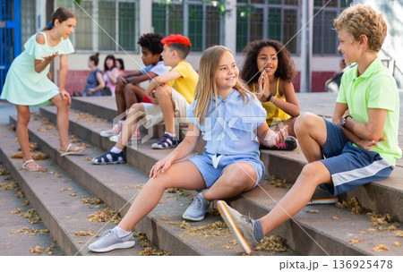 Cheerful preteen girls and boys sitting on steps outdoors and chatting Cheerful preteen girls and boys sitting on steps outdoors and chatting 136925478