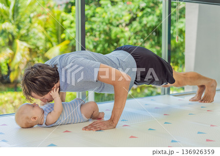 Father exercising with his small baby at home, active parenting and healthy lifestyle. Strong family bond, early physical development, modern fatherhood, fitness with children concept. Father exercising with his small baby at home, active parenting and healthy lifestyle. Strong family bond, early physical development, modern fatherhood, fitness with children concept. 136926359