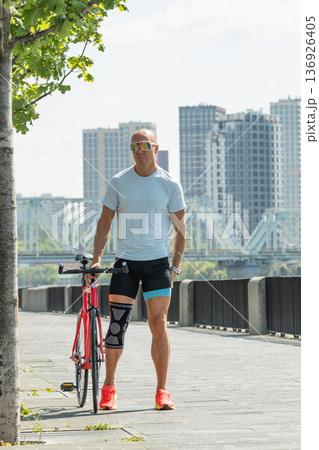 Mature athletic man walking with red bicycle along city embankment 136926405