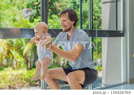 Father exercising with his small baby at home, active parenting and healthy lifestyle. Strong family bond, early physical development, modern fatherhood, fitness with children concept. 136926769