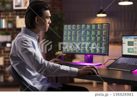 Male business consultant analyzing trading analysis and investment data from home office. Young entrepreneur working remotely, focusing on stock market and financial statistics of startup company. 136926981