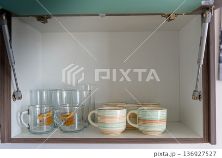 Kitchen cabinet with glass mugs and striped ceramic cups 136927527