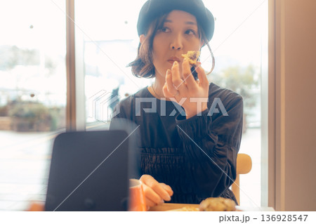 カフェでスマートフォン越しにパンを食べる女性 136928547