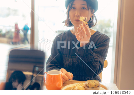 カフェでスマートフォン越しにパンを食べる女性 カフェでスマートフォン越しにパンを食べる女性 136928549
