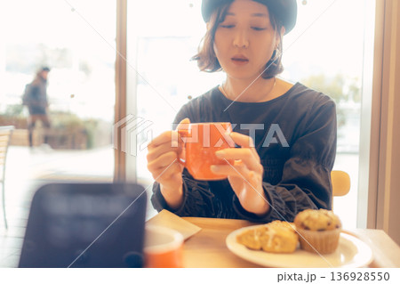 カフェでスマートフォン越しにパンを食べる女性 136928550