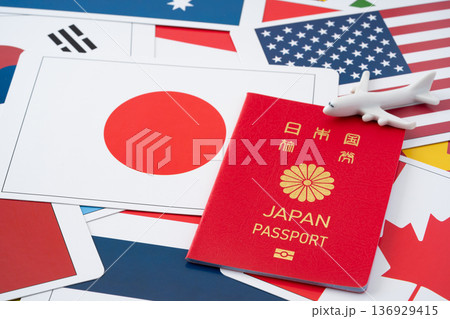 たくさんの国旗のカードを背景に赤い日本のパスポートと飛行機のミニチュア 136929415
