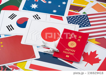 たくさんの国旗のカードを背景に赤い日本のパスポートと飛行機のミニチュア 136929418