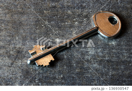 A single antique style metal key lying on a dark, textured rustic surface A single antique style metal key lying on a dark, textured rustic surface 136930547