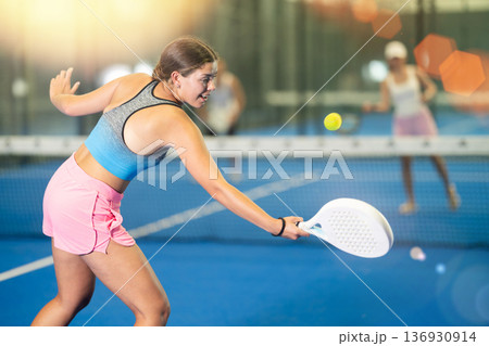 Young woman playing tennis against man and woman 136930914