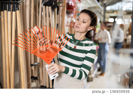 Amateur gardener woman selects necessary items tools for her hobby in greenhouse flower-bed Amateur gardener woman selects necessary items tools for her hobby in greenhouse flower-bed 136930936