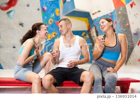 Three friends, man and woman, discuss their climbs on climbing wall without safety net, sitting on bench in recreation area Three friends, man and woman, discuss their climbs on climbing wall without safety net, sitting on bench in recreation area 136931014