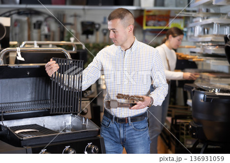 In store, man inspects mobile grill, buys barbecue device 136931059
