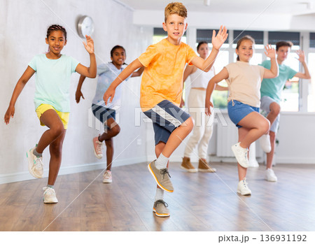 Boy dances vogue in choreographic school, friends and teacher dance in gym blurry background Boy dances vogue in choreographic school, friends and teacher dance in gym blurry background 136931192
