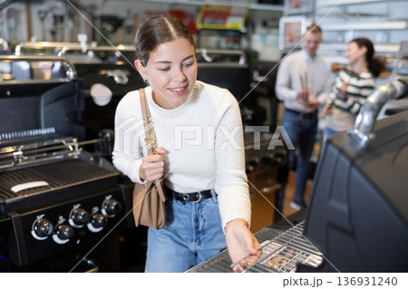 Young woman shopping at garden supermarket - choosing new grill for frying meat Young woman shopping at garden supermarket - choosing new grill for frying meat 136931240