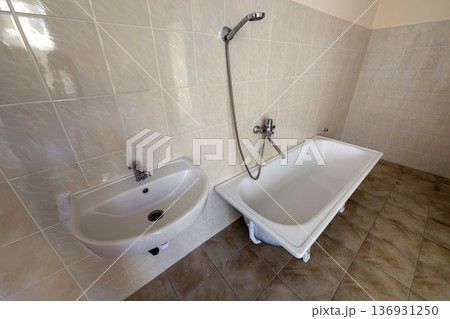 Interior of spacious light hospital or kindergarten bathroom with white bathtub, sink and tiled floor and walls. Interior of spacious light hospital or kindergarten bathroom with white bathtub, sink and tiled floor and walls. 136931250