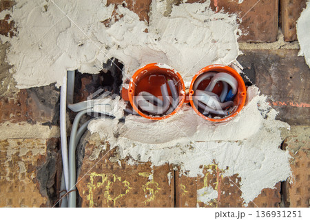 Socket orange boxes with wires in a wall. Cabling installation of electrical wires sticking out from electrical sockets hole on brick wall. 136931251